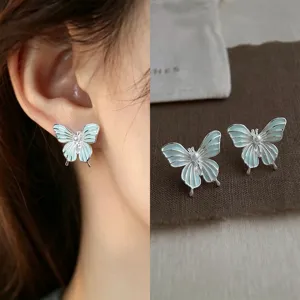 Close-up of blue-green enamel butterfly earrings with pearl centers, shown worn and as a pair