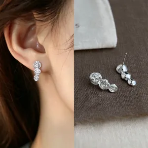 Close-up of a silver three-rose earring worn on the ear, with its matching pair displayed beside it