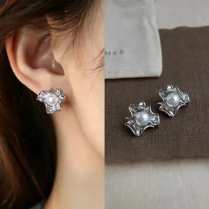 Close-up of a silver folded-petal stud with a white faux pearl, shown worn and laid on fabric