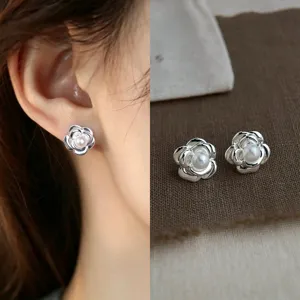 Close-up of layered silver flower studs with pearl centers, worn beside a pair on brown fabric