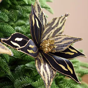 Ornement floral de Noël noir et or, aux pétales rayés, présenté sur des branches de sapin vertes