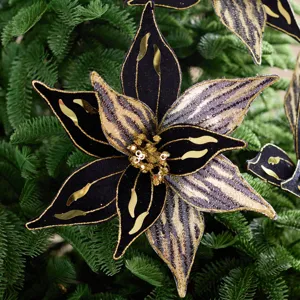 Fleur de Noël artificielle noire et dorée pour sapin, en gros plan parmi des branches vertes