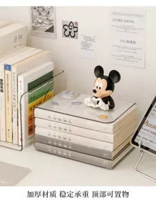 Clear acrylic desktop book organizer holding stacked books, with a small figurine displayed on top