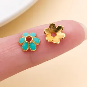 Deux pièces florales en gros plan, l’une émaillée turquoise, l’autre dorée, avec un trou central
