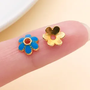 Gros plan de deux pièces métalliques en fleur, bleue émaillée et dorée, avec trous centraux