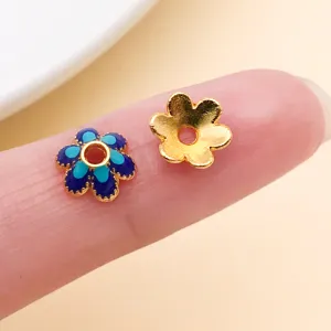 Gros plan sur deux pièces florales, l’une émaillée en bleu, l’autre dorée, avec un trou central.