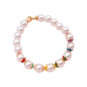 Bracelet de perles imitation blanches, fleurs émaillées multicolores et fermoir doré, posé à plat