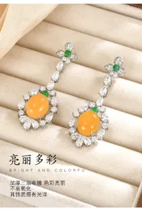 Detalle de cabujones naranjas, piedras claras y toques verdes en pendientes largos plateados