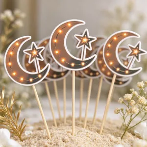 Close-up of crescent moon and star cake toppers with warm glowing lights in a sandy display