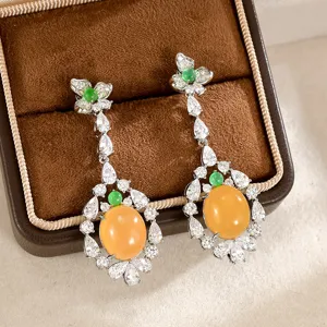 Par de pendientes largos plateados con piedras ovaladas naranja, detalles verdes y circonitas
