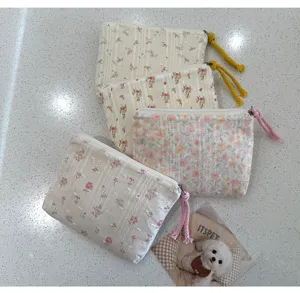 Quatre pochettes fleuries à fermeture zippée et tirettes tressées, posées sur un fond clair