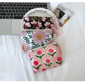 Trois pochettes fleuries zippées superposées sur un linge blanc près d’un ordinateur, vues de dessus