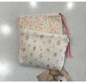 Deux petites pochettes en tissu fleuri, avec fermetures zippées et pompons roses, sont superposées