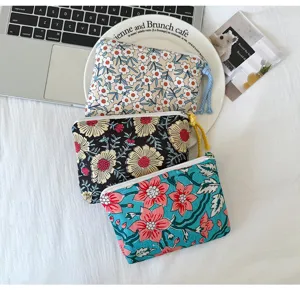 Trois pochettes fleuries zippées, crème, noire et turquoise, avec pompons colorés, disposées à plat