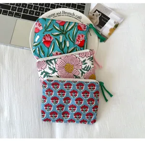 Trois pochettes fleuries zippées avec pompons colorés, disposées à plat et superposées