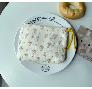 Vue de dessus d'une pochette crème texturée, à fleurs roses, avec tirette de zip tressée jaune
