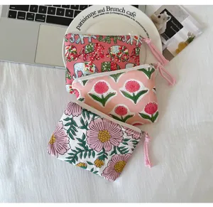 Trois pochettes en coton imprimé, avec zip et pompons, aux motifs floraux et d’éléphants