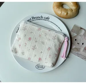 Gros plan sur une pochette fleurie crème, à relief rayé, avec fermeture blanche et pompon rose