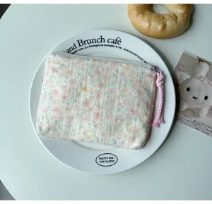 Vue à plat d'une pochette fleurie pastel, zippée, avec cordon rose tressé sur une assiette