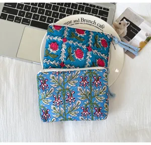 Deux pochettes zippées bleues à motifs floraux, à plat, avec fleurs rouges et feuilles vertes