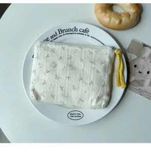 Vue de dessus d’une pochette blanche texturée à fleurs, avec fermeture éclair et tirette jaune tressée