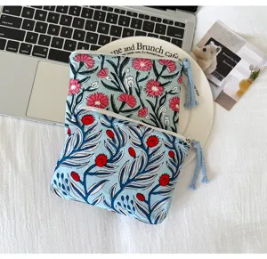 Vue à plat de deux pochettes en tissu bleu clair à fleurs, avec fermeture zippée et tirettes à pompon