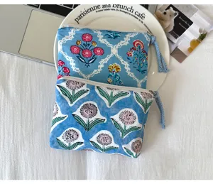 Deux pochettes en coton bleu à motifs floraux différents, avec fermeture zippée et pompons tressés