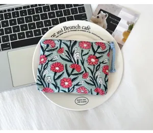 Détail d’une pochette en tissu bleu-gris à fleurs rouges, avec fermeture zippée et pompon tressé