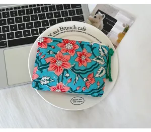 Pochette bleue à fleurs rouges, avec tirette zippée et pompon tissé vert sur une assiette