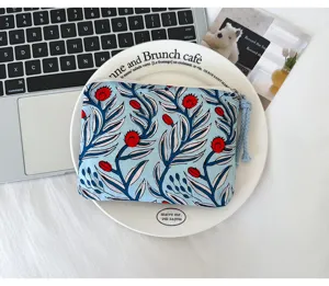 Vue de dessus d’une pochette en tissu bleue à fleurs rouges, avec zip et pompon bleu