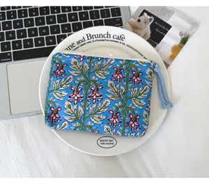 Vue de dessus d’une pochette bleue à motif botanique rouge et vert, avec zip et cordon tressé