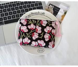 Vue du dessus d’une pochette noire à fleurs roses, avec un pompon rose sur la fermeture éclair