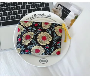 Pochette en tissu noir à fleurs, avec fermeture zippée et pompon jaune, posée sur une assiette