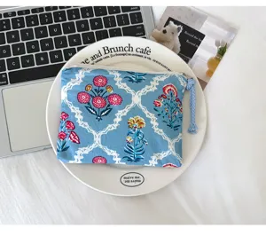 Pochette bleue à fleurs avec zip et pompon tressé, posée sur une assiette blanche, vue de dessus