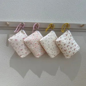 Quatre petites pochettes fleuries en tissu, zippées et munies de cordons tressés, présentées ensemble