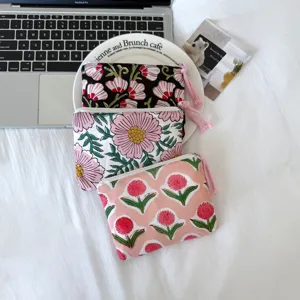 Trois petites pochettes en coton à fleurs, zippées avec tirettes à pompons, présentées sur fond blanc