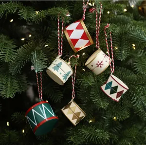 Six patterned drum ornaments hang among evergreen branches, lit by warm lights on striped cords.