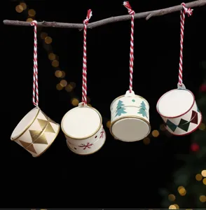 Four patterned metal drum ornaments hang from red-and-white cords against a dark festive backdrop