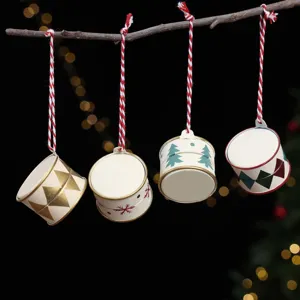 Four miniature hand-painted metal drum Christmas ornaments with festive patterns hang from a branch