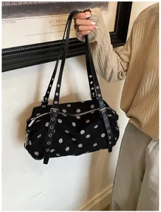 A model holds a black bag with white polka dots, double straps, silver rivets and a zip closure.