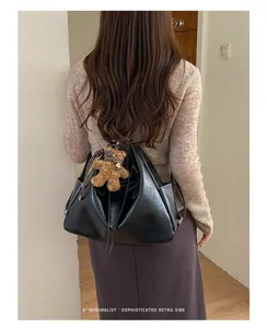Back view of a woman carrying a soft black triangular bag with a teddy bear charm and scarf