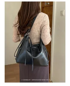 Rear view showing a woman carrying a black shoulder bag with adjustable strap and long tassel