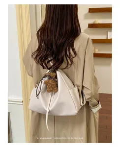 Rear view of an ivory slouchy drawstring bag with a teddy charm, worn over the shoulder