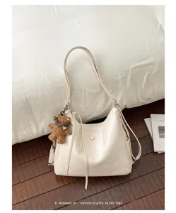 Ivory faux-leather bag with curved silhouette, long straps, snap detail and teddy bear charm
