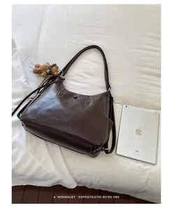 Brown leather-look bag displayed flat with top handle, crossbody strap, and small bear charm