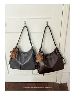 Two dark gray and brown bags hang on a white door, each with long straps and a plush bear charm