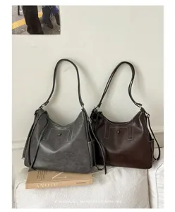 Two leather-look shoulder bags in gray and dark brown displayed side by side on a light sofa