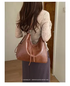 Brown leather-look bucket shoulder bag with long straps and tassel detail, worn on a model