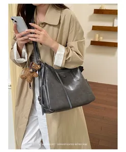 Large gray faux leather shoulder bag with slim straps and a brown teddy bear charm, worn crossbody