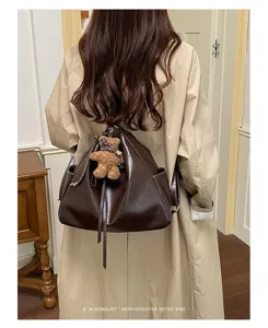 Brown faux leather drawstring backpack tote worn on the back, with a teddy bear charm
